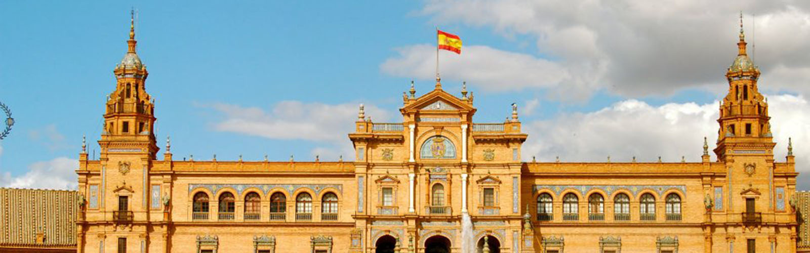 A tan government building with an ornate facade, two small towers, and a Spanish flag.